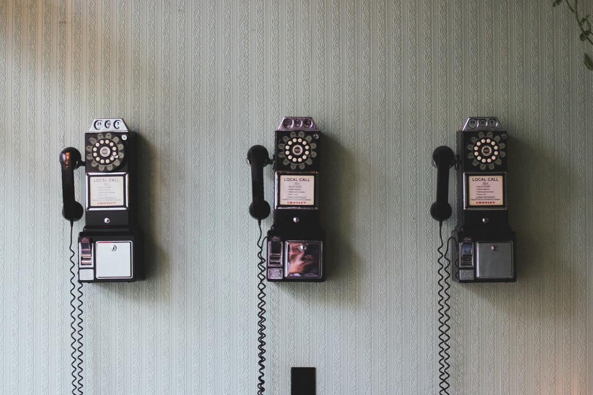 Three vintage wall-mounted payphones with curly handset cords.